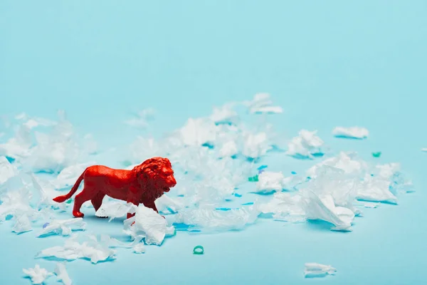 青い背景にプラスチック片を持つ赤いおもちゃのライオン 環境汚染の概念 — ストック写真