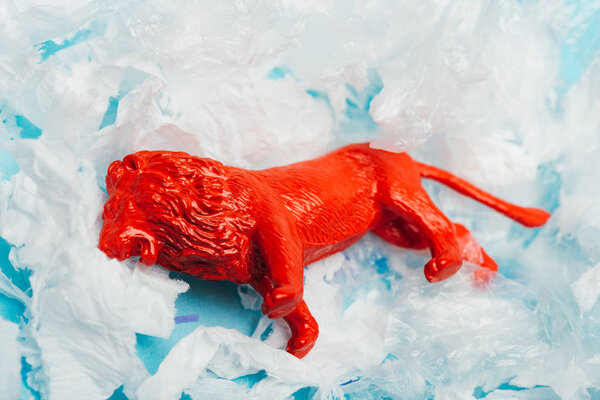 Red toy lion on plastic garbage on blue background, animal welfare concept