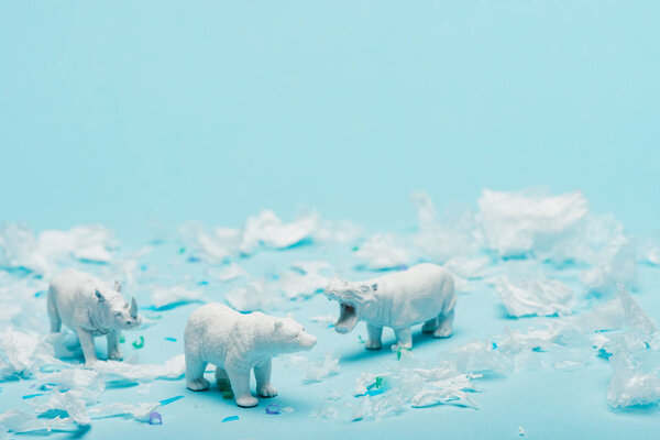 White toys of hippopotamus, rhinoceros and bear with plastic garbage on blue background, animal welfare concept