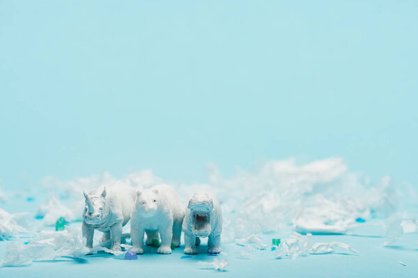 White toys of hippopotamus, rhinoceros and bear with plastic garbage on blue background, animal welfare concept