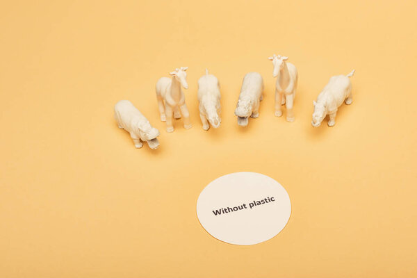 Белые игрушки животных с надписью без пластика на карточке на желтом фоне, концепция загрязнения окружающей среды
