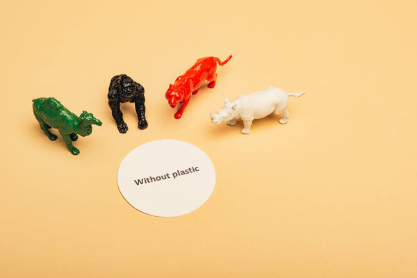 Цветные игрушки животных с надписью без пластика на карточке на желтом фоне, концепция загрязнения окружающей среды
