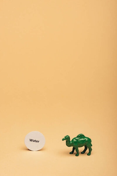 Green toy camel with lettering water on card on yellow background, water scarcity concept