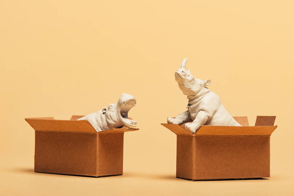 White toy hippopotamus and rhinoceros in cardboard boxes on yellow background, animal welfare concept