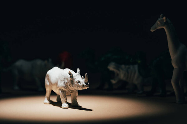 White toy rhinoceros under spotlight with animals at background, voting concept