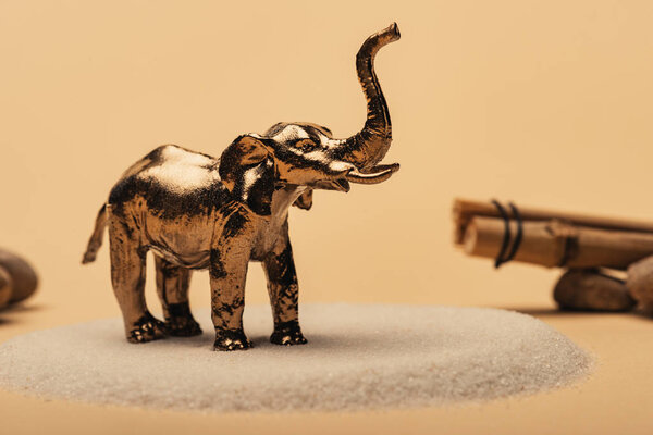 Selective focus of toy elephant on sand with stones and wooden sticks on yellow background, animal welfare concept
