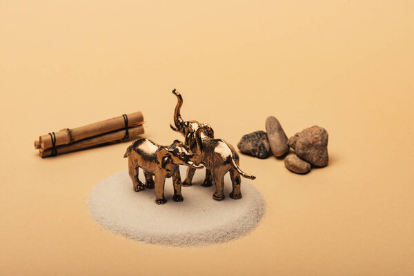 Toy elephants on sand with stones and wooden sticks on yellow background, animal welfare concept
