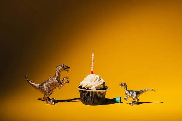 Игрушечные Динозавры Кепкой Вечеринок Рядом Кексом Свечой Оранжевом Фоне — стоковое фото