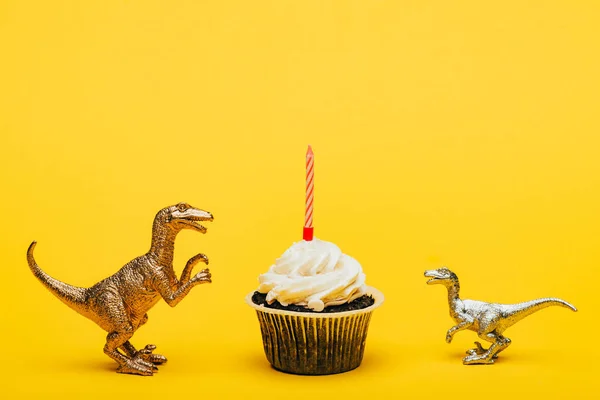 stock image Toy dinosaurs beside cupcake with candle on yellow background