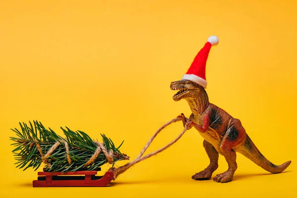 Mainan Dinosaurus Topi Santa Dengan Pinus Giring Pada Latar Belakang — Stok Foto