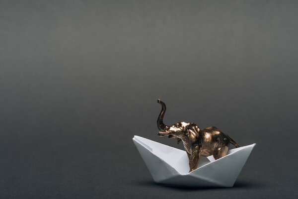 Golden toy elephant in paper boat on grey background, animal welfare concept
