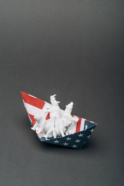 White toy animals in paper boat from american flag on grey background, animal welfare concept