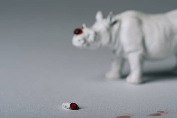 Селективный фокус рога с кровью и игрушечными носорогами на сером фоне, охота за концепцией рога
