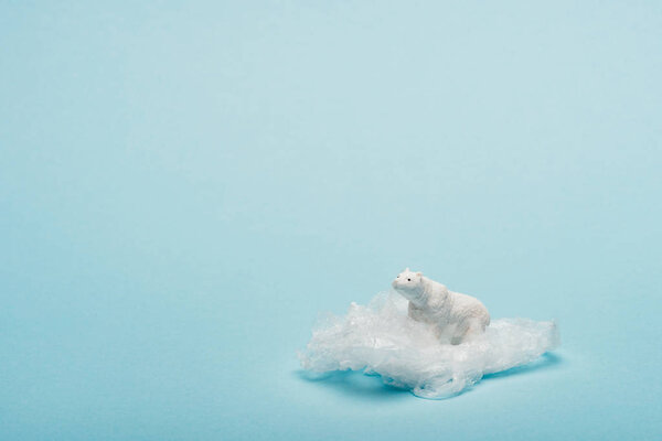 Toy polar bear on plastic packet on blue background, environmental pollution concept