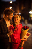 lächelnder Mann umarmt glückliche Freundin mit Rosenstrauß und Karte mit Liebesaufschrift und Herzsymbol