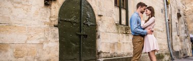 panoramic shot of young couple embracing while standing near old stone castle clipart