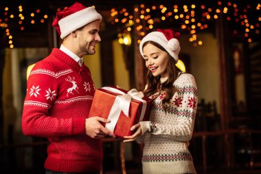 Şaşkın sevgiliye Noel hediyesini sunan neşeli adam.
