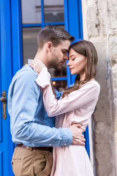 青いドアの近くに顔を出しながら抱き合う幸せな若いカップル — ストック写真