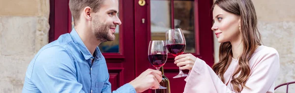 坐在街边咖啡店里的一对笑容满面的情侣的全景照片 还有叮当声的红酒 — 图库照片