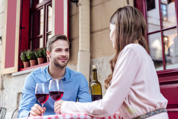 happy young couple sitting in street cafe with glasses of red wine
