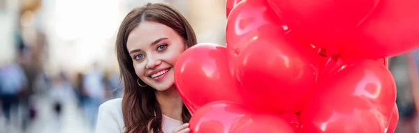 Güzel Bir Kızın Kırmızı Kalp Şeklindeki Balonları Tutarken Kameraya Gülümsediği — Stok fotoğraf