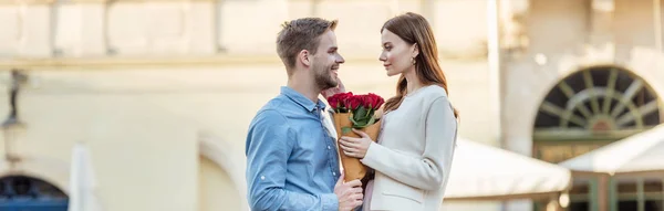 panoramic shot of handsome man presenting bouquet of roses to beautiful girlfriend on street