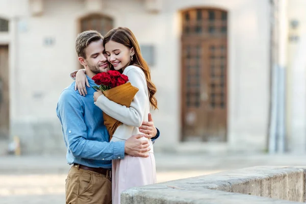 在街上牵着一束玫瑰时 快乐的女孩与男朋友拥抱在一起 — 图库照片