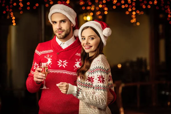 快乐的年轻夫妇戴着圣诞礼帽 拿着香槟酒杯和火焰喷射器看着镜头 — 图库照片