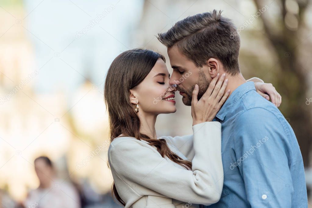 happy girl with closed eyes kissing handsome boyfriend on street