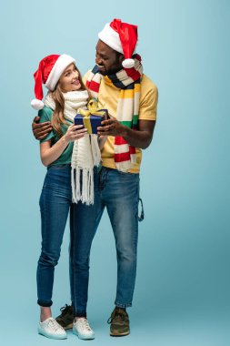 Noel Baba şapkalı ve eşarplı mutlu Afro-Amerikan erkeği kız arkadaşına hediye ediyor.