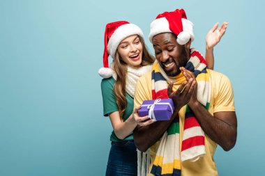 Mutlu kız Noel Baba şapkası ve eşarp hediye afro amerikan erkek arkadaşı mavi izole