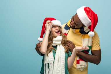Mutlu ırklar arası çiftler Noel Baba şapkaları ve eşarpları içinde yalnızken eğleniyorlar.