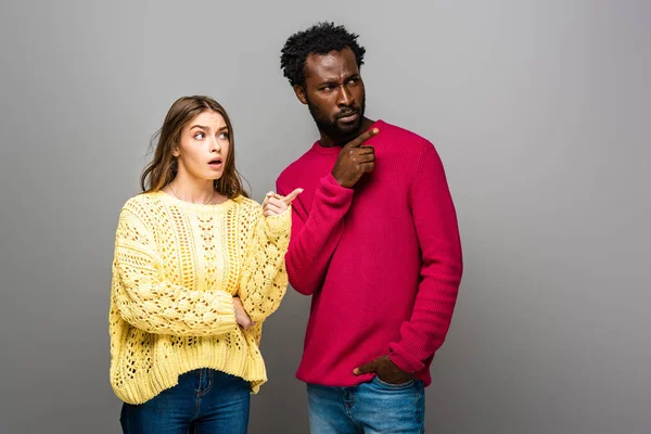 Shocked Interracial Couple Knitted Sweaters Pointing Fingers Grey Background — Stock Photo, Image