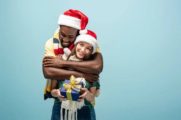 Gelukkig Interraciaal Paar Santa Hoeden Sjaals Knuffelen Houden Geschenk Doos — Stockfoto