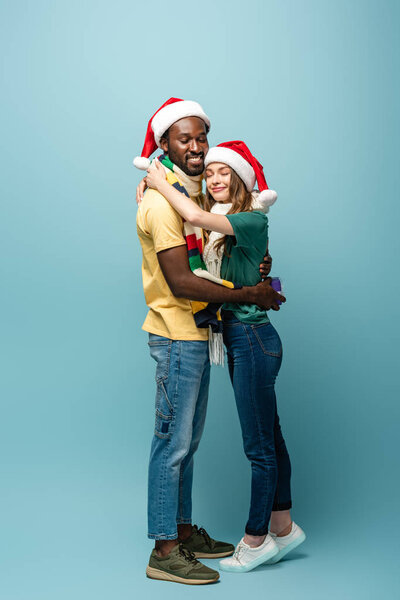 happy interracial couple hugging with present on blue background