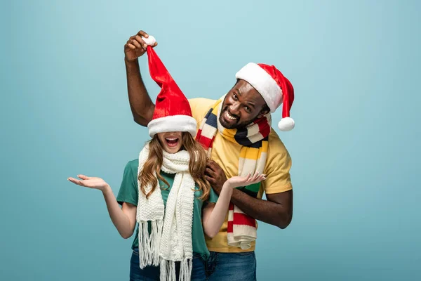 Feliz Interracial Pareja Santa Sombreros Bufandas Divertirse Aislado Azul —  Fotos de Stock