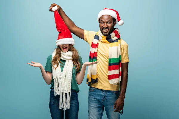 Feliz Interracial Pareja Santa Sombreros Bufandas Divertirse Aislado Azul —  Fotos de Stock