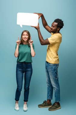 Afrikalı Amerikalı bir adam, kız arkadaşının üzerinde konuşma balonu tutuyor mavi arka planda fikir jesti yapıyor.