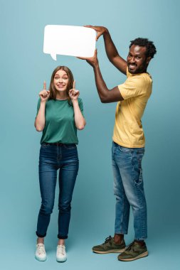 Afrikalı Amerikalı bir adam, kız arkadaşının üzerinde konuşma balonu tutuyor mavi arka planda fikir jesti yapıyor.