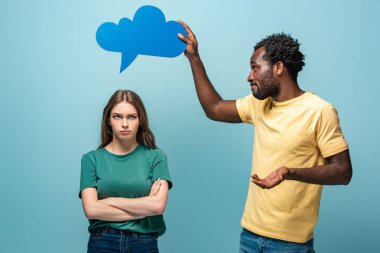 african american man holding thought bubble above offended girlfriend on blue background clipart