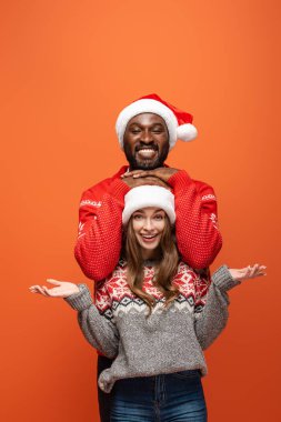 Noel Baba şapkalı mutlu bir çift ve turuncu arka planda Noel süveteri.