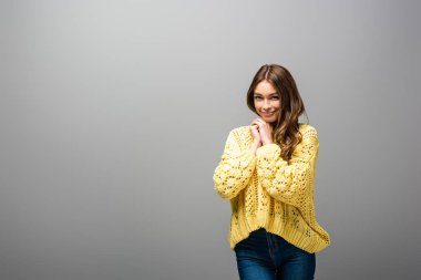 Gülümseyen utangaç kadın gri arka planda sarı kazak giyiyor.