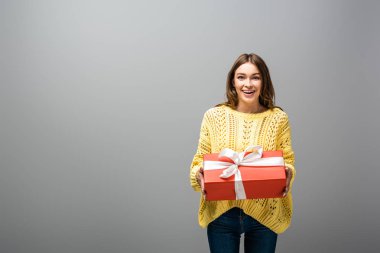Heyecanlı, mutlu, sarı kazaklı bir kadın gri arka planda hediye kutusu tutuyor.