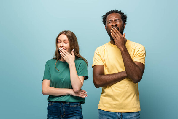 sleepy interracial couple yawning on blue background