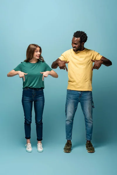 Feliz Casal Interracial Apontando Com Dedos Para Baixo Fundo Azul — Fotografia de Stock