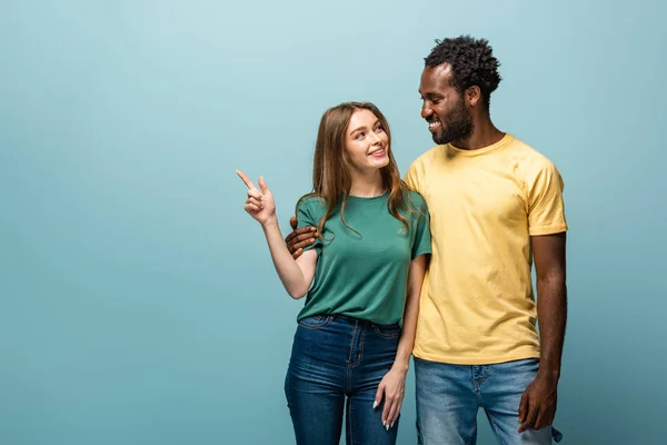 Sorrindo Casal Interracial Apontando Com Dedo Afastado Fundo Azul — Fotografia de Stock