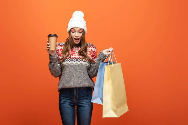 冬服のショッピングバッグやコーヒーを持ってオレンジの背景に行くためにショックを受けた女の子 — ストック写真