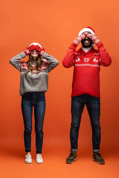 Happy Interracial Couple Santa Hats Mittens Christmas Sweaters Covering Eyes — Stock Photo, Image