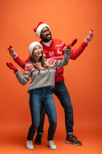 Happy Interracial Couple Santa Hats Mittens Christmas Sweaters Outstretched Hands — Stock Photo, Image