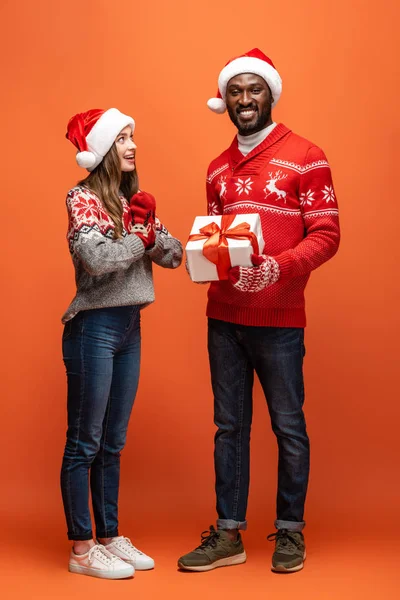 Hombre Afroamericano Regalando Regalo Navidad Novia Feliz Sobre Fondo Naranja —  Fotos de Stock